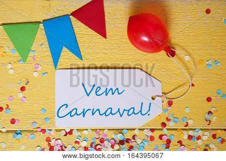 White Label With Spanish Text Vem Carnaval Means Happy Carnival. Party Decoration Like Streamer, Confetti And Balloon. Flat Lay Or Top View. Yellow Wooden Background