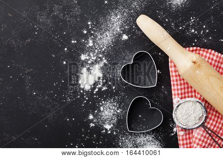 Baking background with flour, rolling pin and heart shape on kitchen black table top view for Valentines day cooking. Flat lay style.