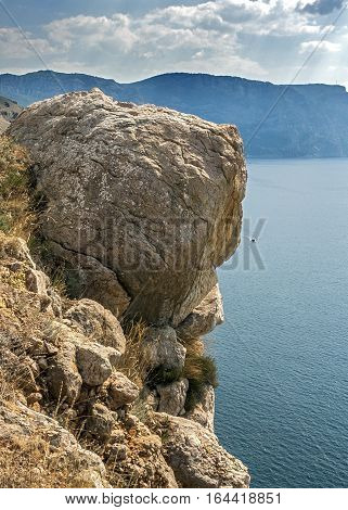Russia Crimea. Rocks which snap into the sea near Balaklava. Hot Crimean sun-scorched grass rare green bushes mozhevelnik. Huge boulders miraculously hold on a slope.
