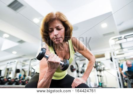 Senior woman in sports clothing in gym working out with weights. Close up of hands.