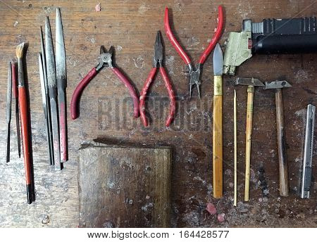 Gold maker tools which are hammer cutter pliers pincers forceps tongs metal file rasp sharpen hone whet halfround file cutter paint brush and wooden plate with trail of melten plastic