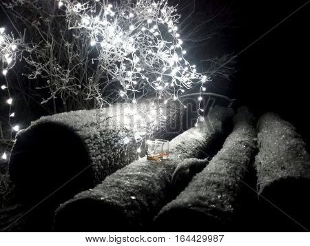 Two whiskey glasses on timber surrounded by lights in winter