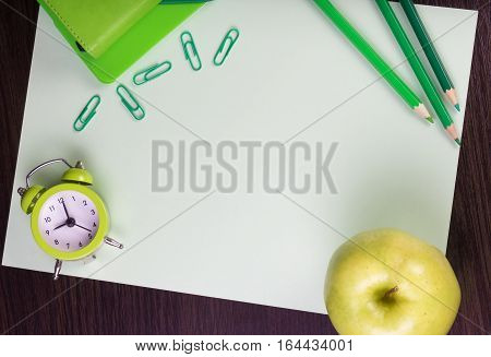 Paper sheet stationery clock and apple on dark wooden background. Different tints of green. Top view. Can be used as a field for notes notebook cover.