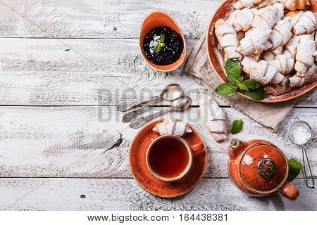 Rugelach with jam filling on plate with tea on white wooden background, top view with copy space