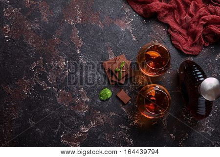 Two glasses of brandy or cognac and bottle with chocolate on dark background. top view with copy space