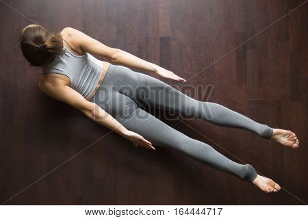 Beautiful young model working out in home interior, doing yoga or pilates exercise on wooden floor. Double Leg Kicks, Salabhasana, Locust pose. Top view. Full length