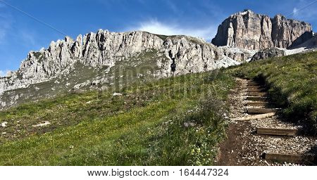 beautiful panorama of Piccolo Pordoi and Sass Pordoi with meadow and hiking trail bellow with blue sky during hiking from Passo Pordoi to Piz Boe peak in Dolomites