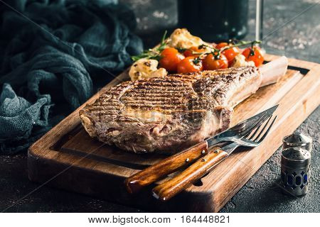 Succulent grilled tomahawk beef steak on the bone with red wine, seasonings, fresh rosemary and grilled vegetables on cutting board