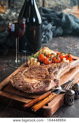Succulent grilled tomahawk beef steak on the bone with red wine, seasonings, fresh rosemary and grilled vegetables on cutting board