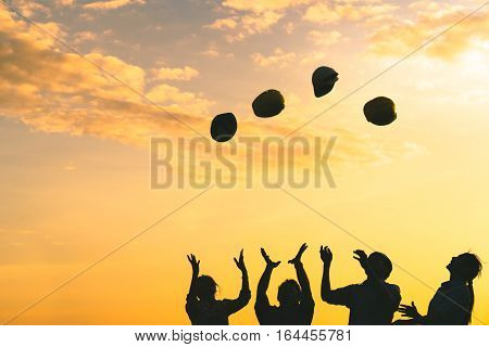 Silhoutte of construction engineers throwing safety helmets upward on golden sunset sky multiethnic diverse group engineering industry or success teamwork celebration concept