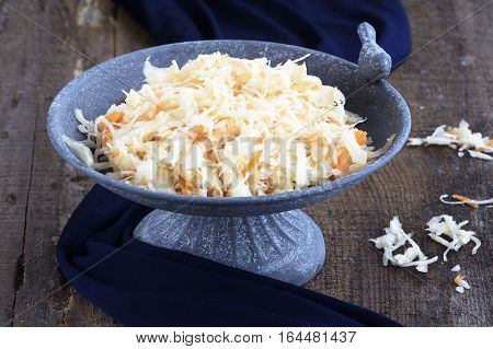 Homemade Sauerkraut with carrots in an elegant stone plate with a bird on a rough wooden background with dark blue cloth. On the table is scattered sauerkraut.