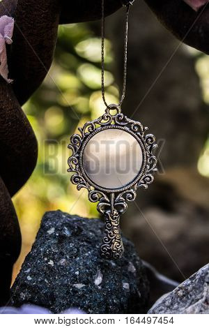 Small magic mirror hanging in a bow with rocks underneath.
