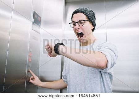 Young stylish guy standing in elevator. He is looking at his watch and begins to understand he is late. Unfortunately he has a panic attack. Poor boy is screaming