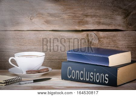Conclusions. Stack of books on wooden desk.