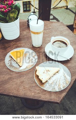 Top view two coffee cups with piece of white new york cheesecake and orange cake on brown wooden table outdoor street cafe. Funky Latte John Glass fever and classic americano. Copy space