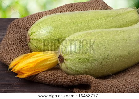 two courgettes with a flower on sackcloth and wooden background.
