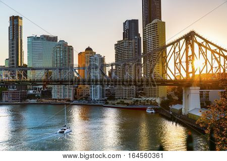 Yacht passing under Brisbane Story Bridge as the sunsets behind the cityscape