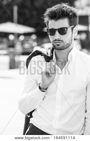Handsome sexy man outdoors. Elegant and sensual. Sunglasses. legance and beauty. Outdoor. Black and white. The young man wears a white shirt.