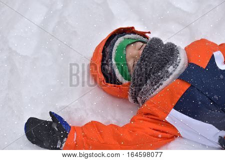 Funny little kid boy in colorful clothes playing outdoors during snowfall in winter on cold snowy days. Happy child having fun and playing with snow