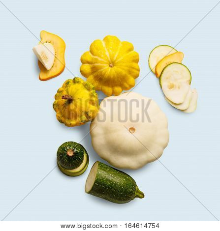 Yellow, white and green zucchini, courgette and round pattipan squashes on blue background. Sorts of cucurbit top view