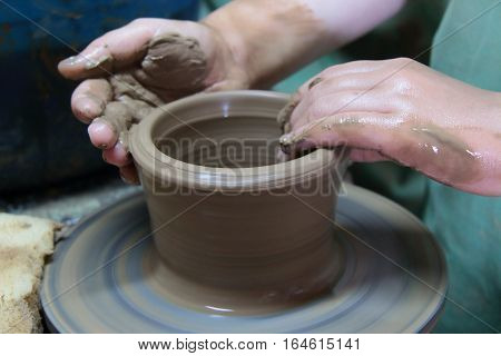 hands of a potter, creating an earthen jar on a pottery wheel
