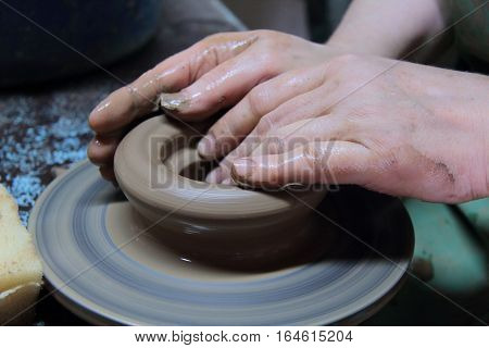 hands of a potter, creating an earthen jar on a pottery wheel