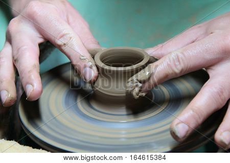 hands of a potter, creating an earthen jar on a pottery wheel