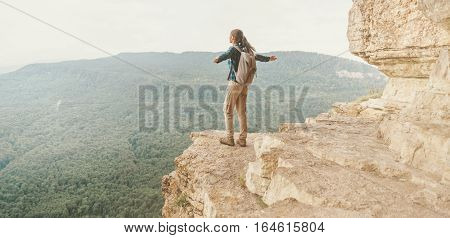 Backpacker young woman standing on cliff Eagle shelf with raised arms and enjoying view of nature Mezmay Krasnodar region Russia