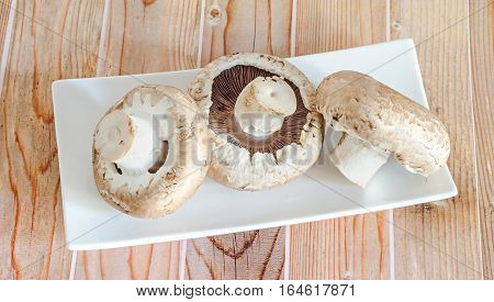 Mushrooms Champignon, Agaricus Bisporus On A White Plate, Close Up, Wood Background.