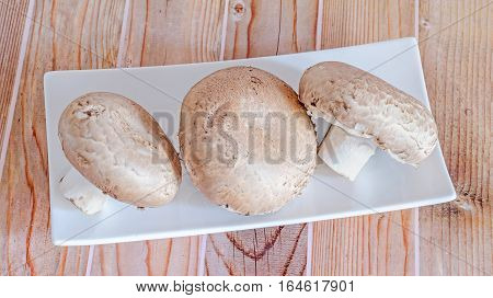 Mushrooms Champignon, Agaricus Bisporus On A White Plate, Close Up, Wood Background.