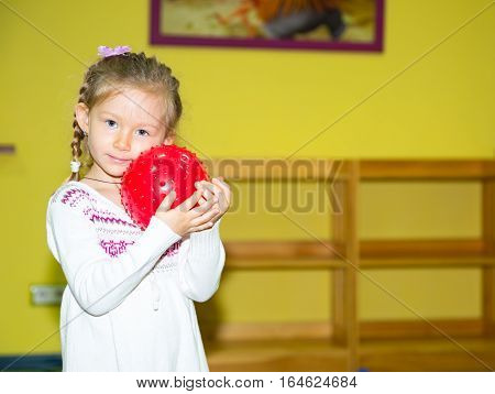Little child girl playing with ball in kindergarten in Montessori preschool Class. Adorable kid in nursery room.