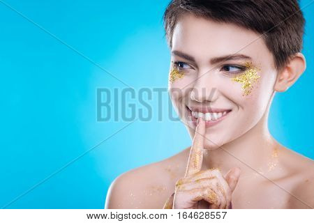 True emotions. Pleasant cheerful model amiling and looking aside while standing on blue background