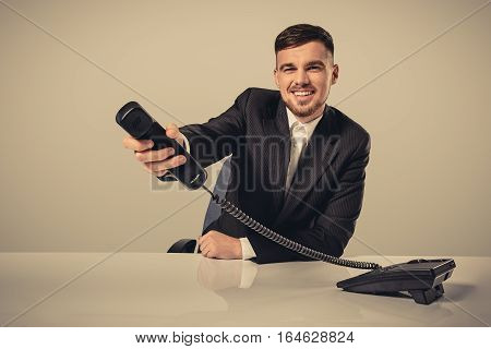 Portrait of attractive businessman holding telephone in his hand. This call is for you concept. A young man in a black suit dials the phone number while sitting in the office