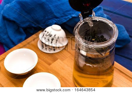 Green herbal tea in glass teapot on the blue wood background with tea cup