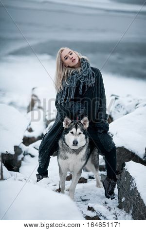 Girl with dog Malamute among rocks in winter. She sits astride dog among rocks.
