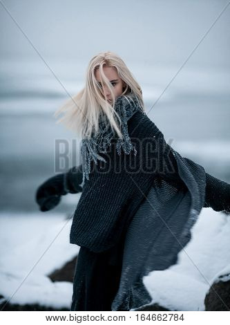 Girl in snow on winter background. She stands and wind blowing her hair.