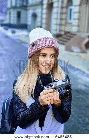 Beautiful girl photographer photographing the old town with retro camera. She is wearing a knitted cap
