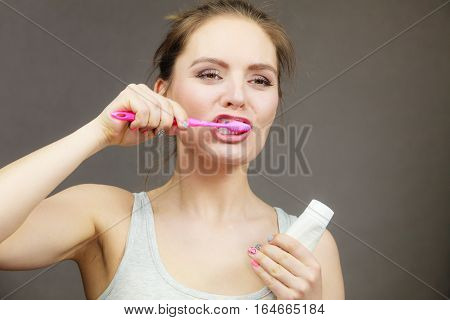 Woman holding brush and tooth paste for teeth cleaning. Happy funny smiling girl with toothbrush. Oral hygiene. Studio shot dark background