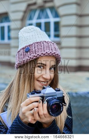 Beautiful girl photographer photographing the old town with retro camera. She is wearing a knitted cap