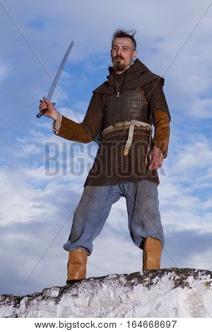 Knight on a rock with a sword against blue cloudy sky