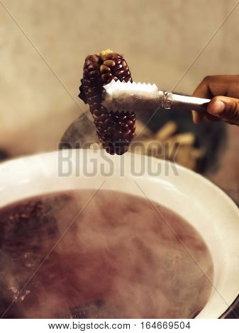 purple waxy corns are boiled in the basin Use a fork to fork corn from the boiling water.