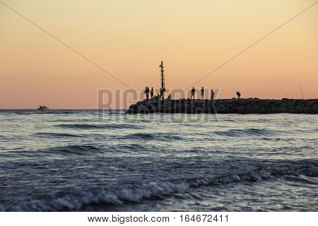 Sunset on Tyrrhenian sea, view of breakwater, fishermen silhouettes, harbor and seacoast of Terracina, Lazio, Italy