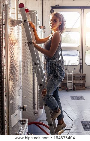 Female Winemaker Controls The Quality Of Wine On Ladder Over Tank
