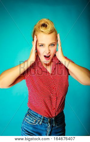 Shocking amazed astonished gestures concept. Shocked lovely pin up young girl holding head with hands. Studio shot on blue background