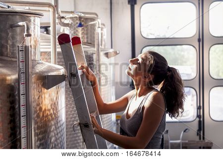 Female Winemaker Controls The Quality Of Wine On Ladder Over Tank