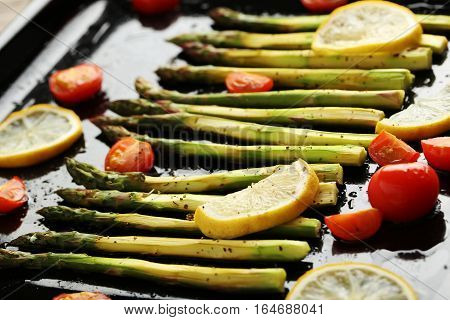 Fresh Baked Asparagus With Lemons And Tomatoes On Black Pan