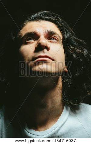 Portrait of a handsome young man with long hair looks up closeup