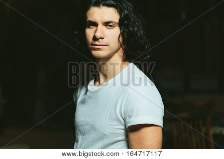 Portrait of a beautiful brutal guy with long hair on a dark background