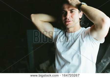 Beautiful long-haired brunette guy hands behind his head in white t-shirts