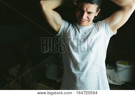 Beautiful long-haired brunette guy hands behind his head in white t-shirts